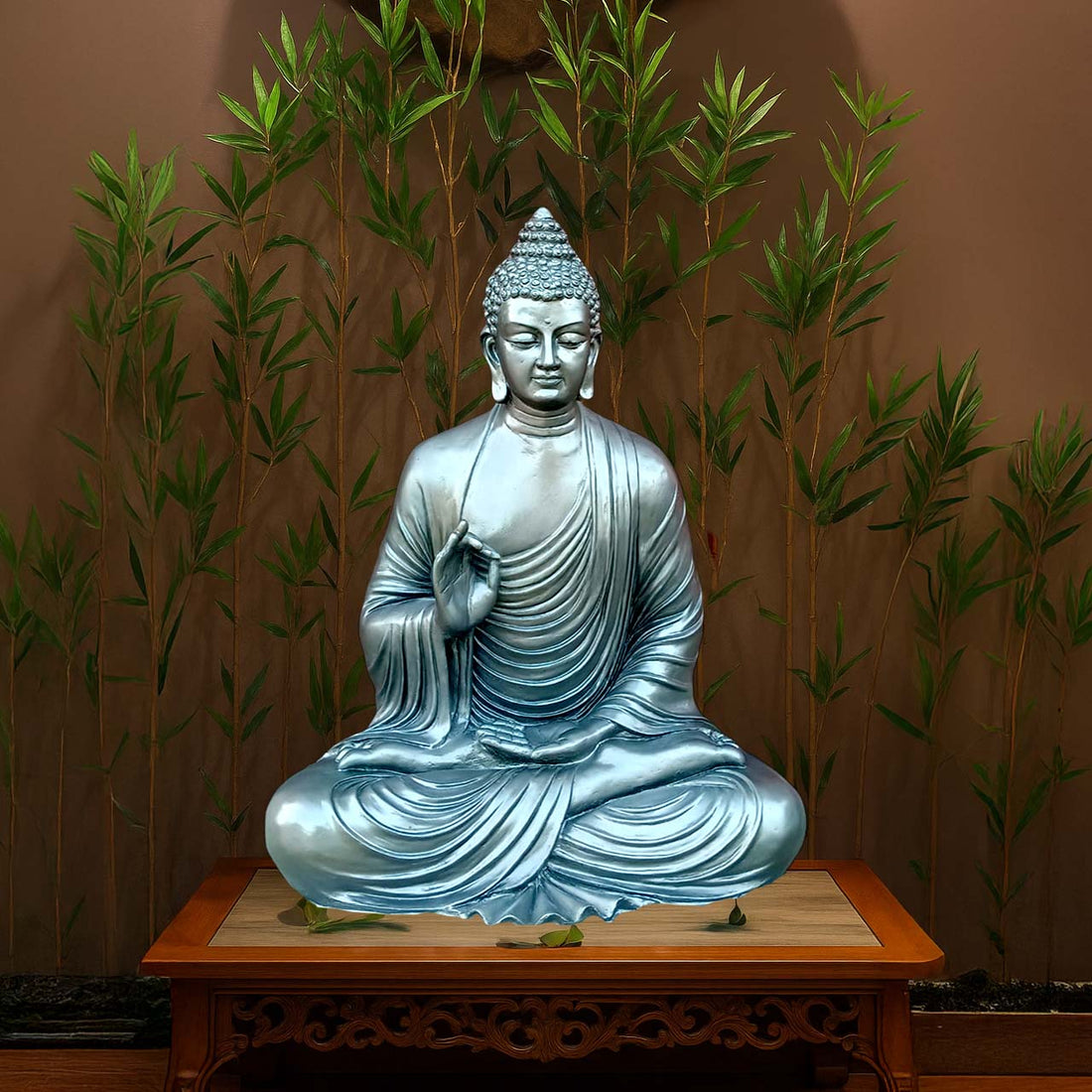 Serene meditating Buddha sculpture in a metallic silver-blue finish, seated in lotus posture on a carved wooden pedestal, with bamboo plants in the background for a peaceful setting.