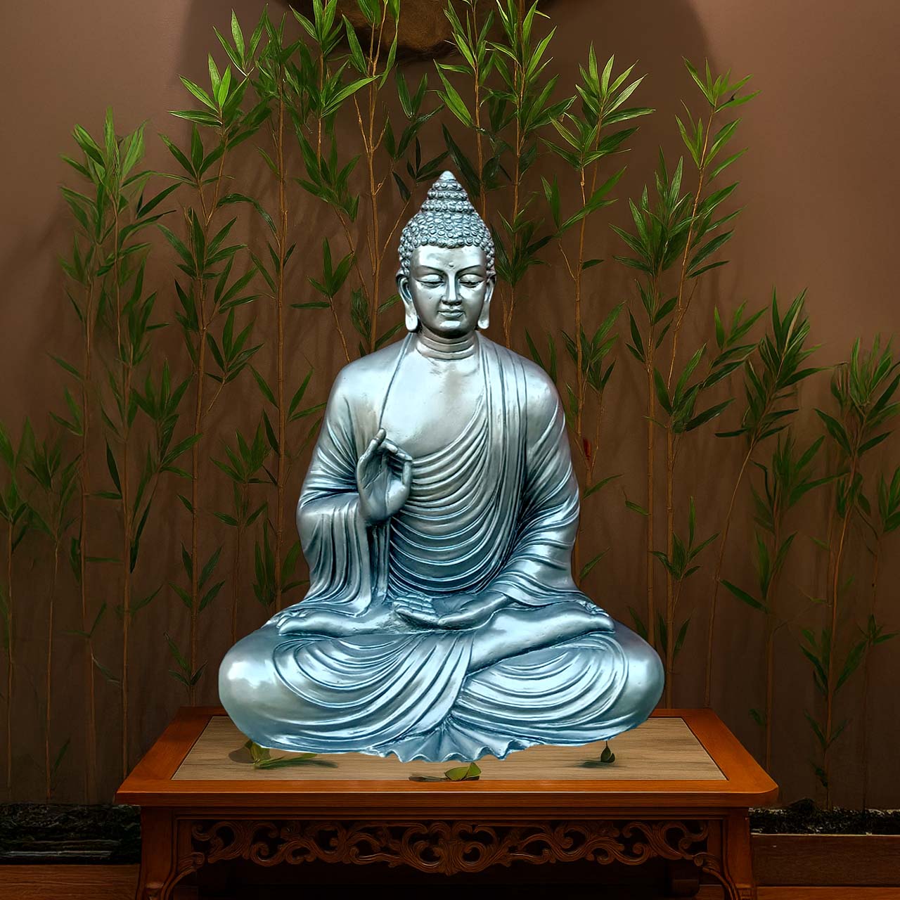 Serene meditating Buddha sculpture in a metallic silver-blue finish, seated in lotus posture on a carved wooden pedestal, with bamboo plants in the background for a peaceful setting.