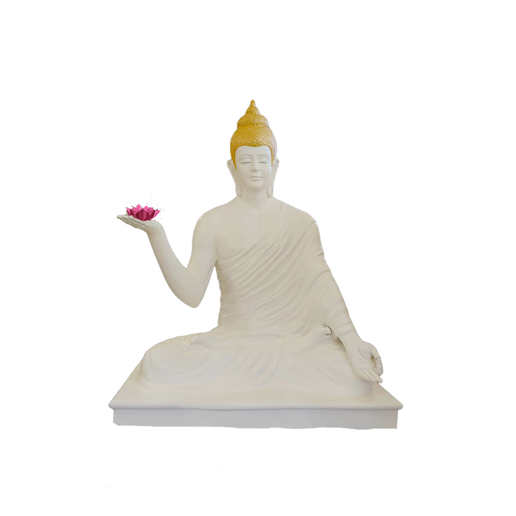 Peaceful white Buddha statue with golden crown, seated in meditation pose and holding a pink lotus, placed in a landscaped garden with lush greenery and flowers.